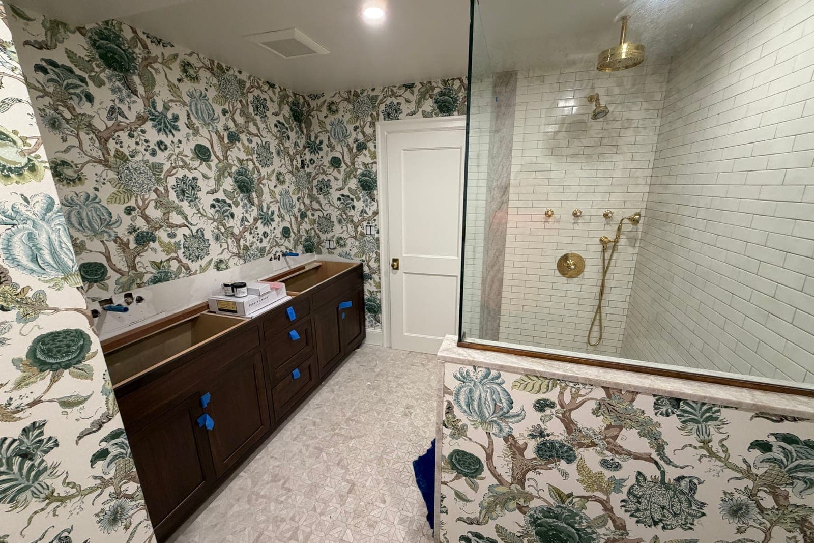 Bathroom mid-renovation: floral chintz paper up, the vanity still taped and the sinks not yet set