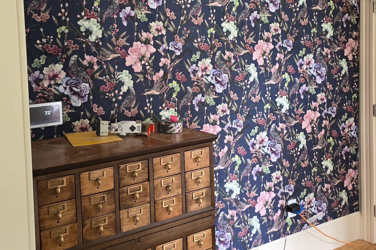 Dark floral paper behind an antique dresser, tools still on top