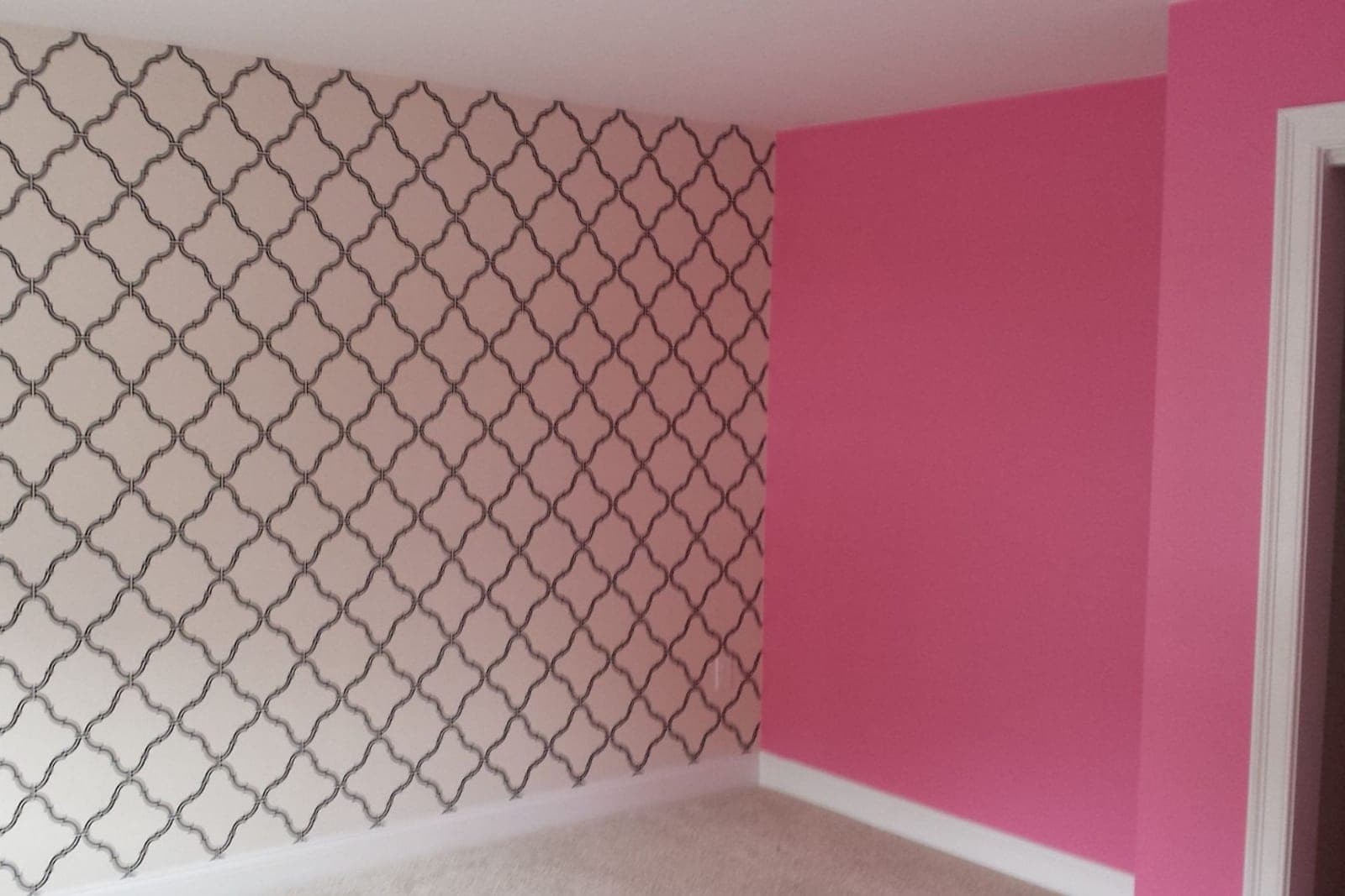 A grey quatrefoil paper on one wall of a pink room before furniture