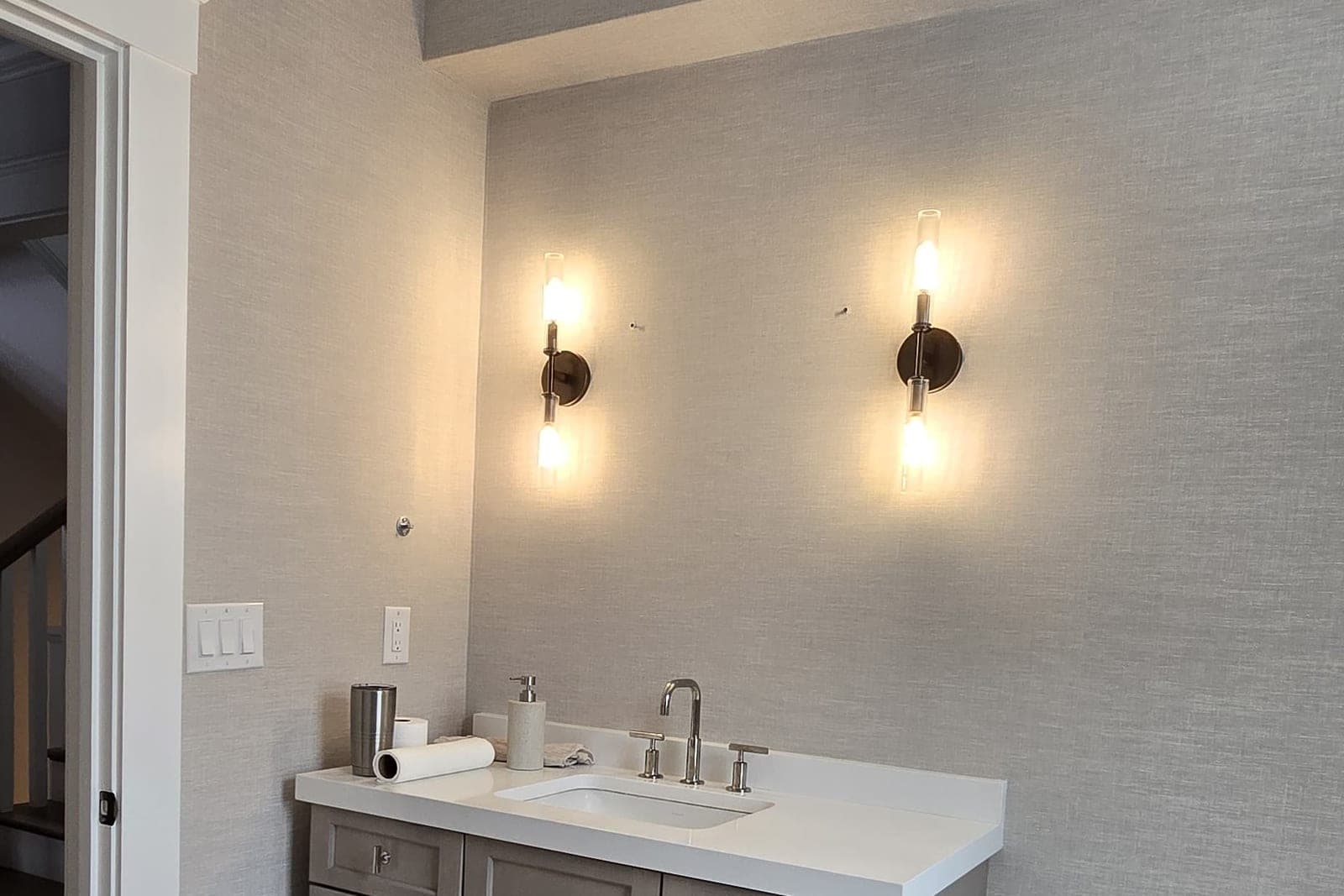 Bathroom in soft grey grasscloth with a pair of sconces over a white vanity