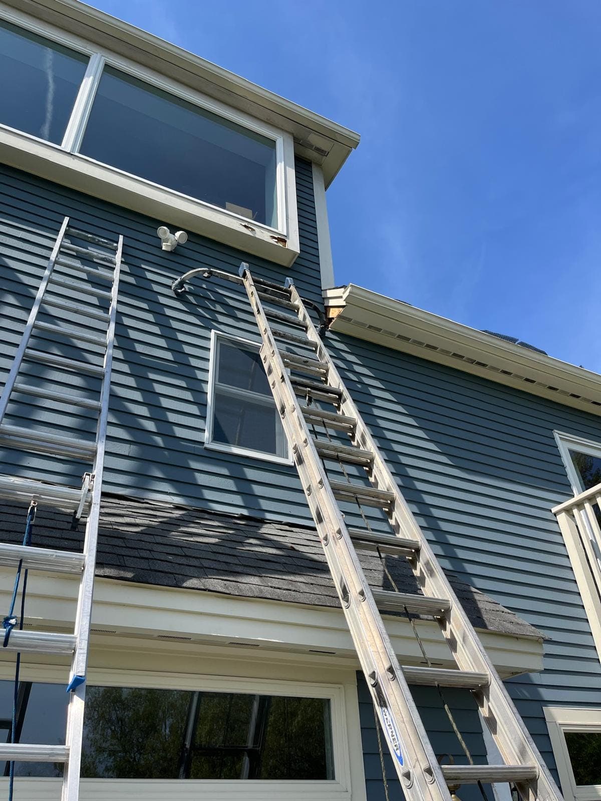 A ladder reaching the gable of a blue clapboard house under a clear sky