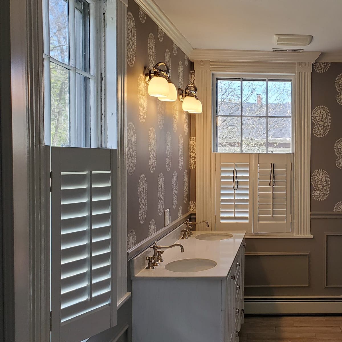 Powder room in a grey medallion print with plantation shutters and a white vanity